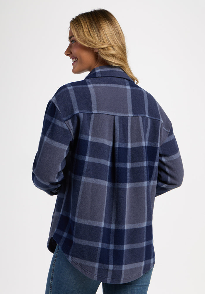 Woman in Woolx Sawyer Shacket - Midnight Harbor Plaid, smiles with hands in pockets, facing away against plain background.