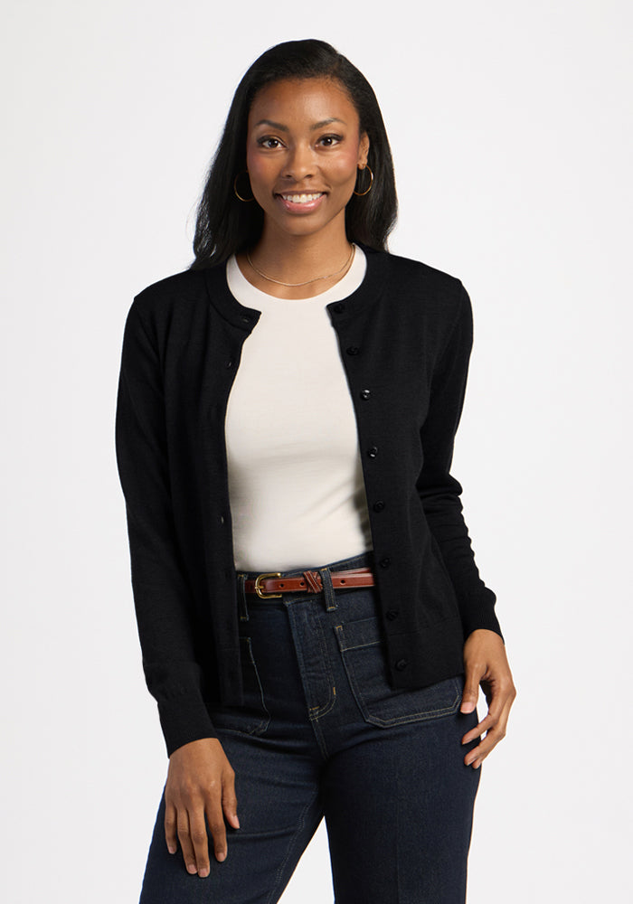 Woman smiling in Woolx Caitlin Sweater - Black, white shirt, blue jeans, and a brown belt against white. 