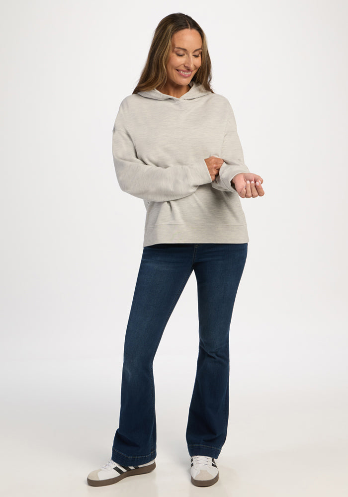 A woman wears a light ash Genevieve Hoodie with dark blue flared jeans and sneakers.