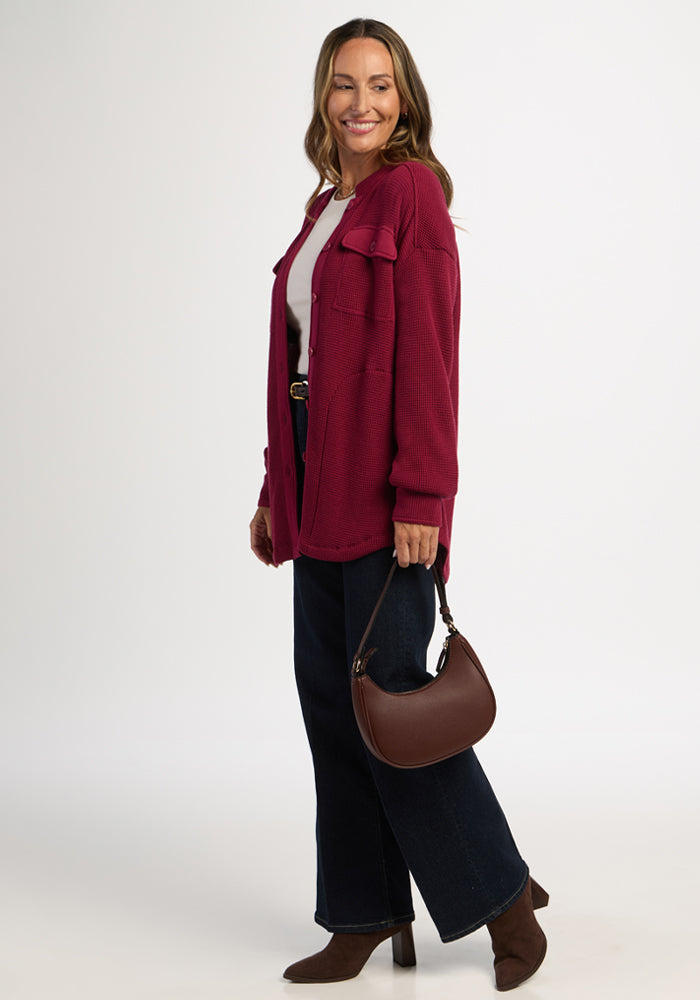 Woman in Woolx Oaklynn Waffle Shacket in Beet Red, white top, dark jeans, boots, holding a brown handbag, smiling.