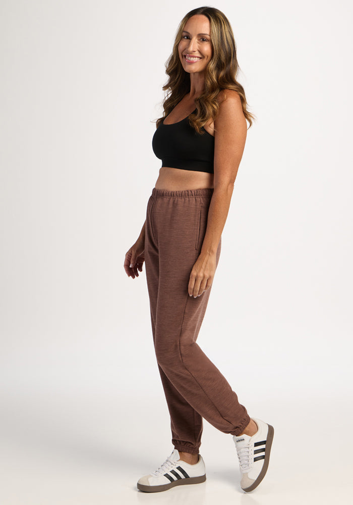 Woman in a black crop top and Woolx Juliette Joggers - Sable Heather smiles, standing against a white background.