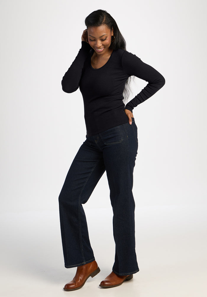 Woman smiles, touching her hair in Woolx Katie Ribbed Long Sleeve - Black, jeans, and brown boots.