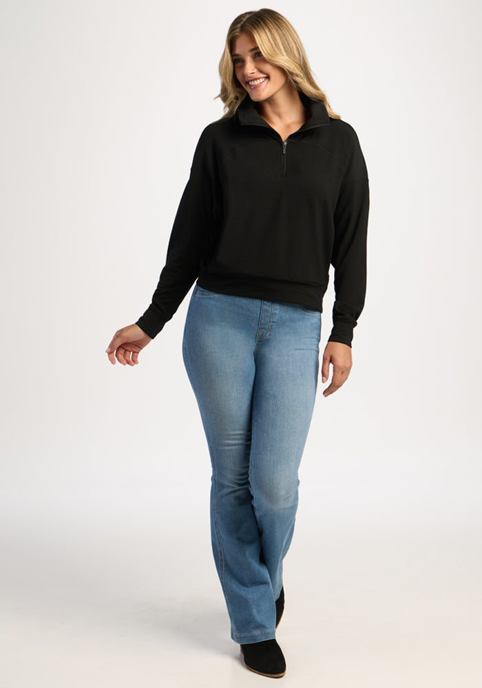 A woman wears a black Woolx Tori 1/4 Zip and light-wash blue jeans.