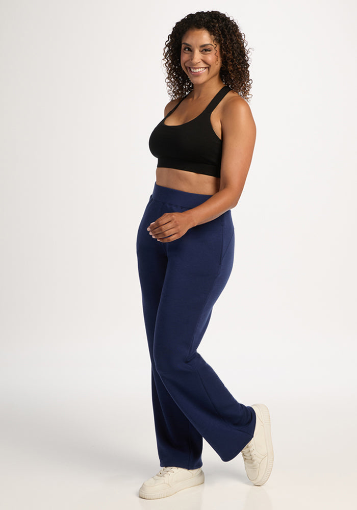 Woman stands smiling in Bree Lounge Pants - Ocean Cavern by Woolx, a black crop top, and white sneakers.