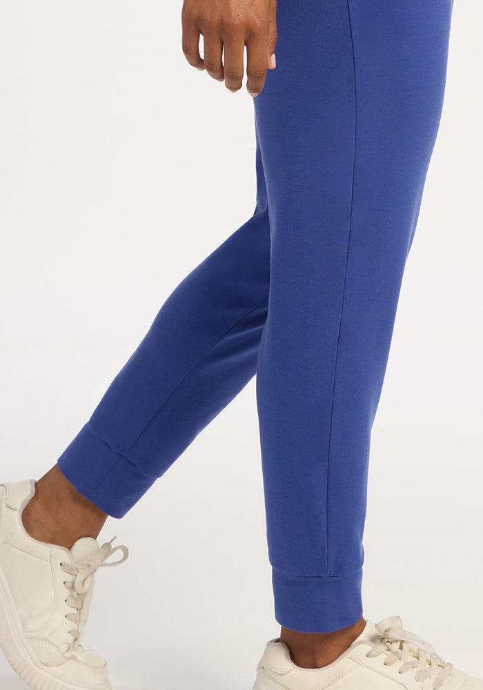 Someone wears Woolx Madden Petite Joggers in royal blue with white sneakers, standing on a white background.