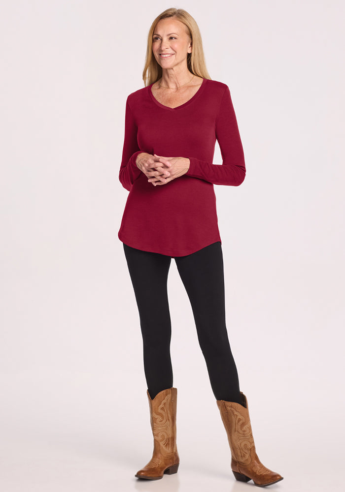 Woman in Woolx Eva Petite Tunic - Beet Red, black leggings, brown cowboy boots, standing and smiling.