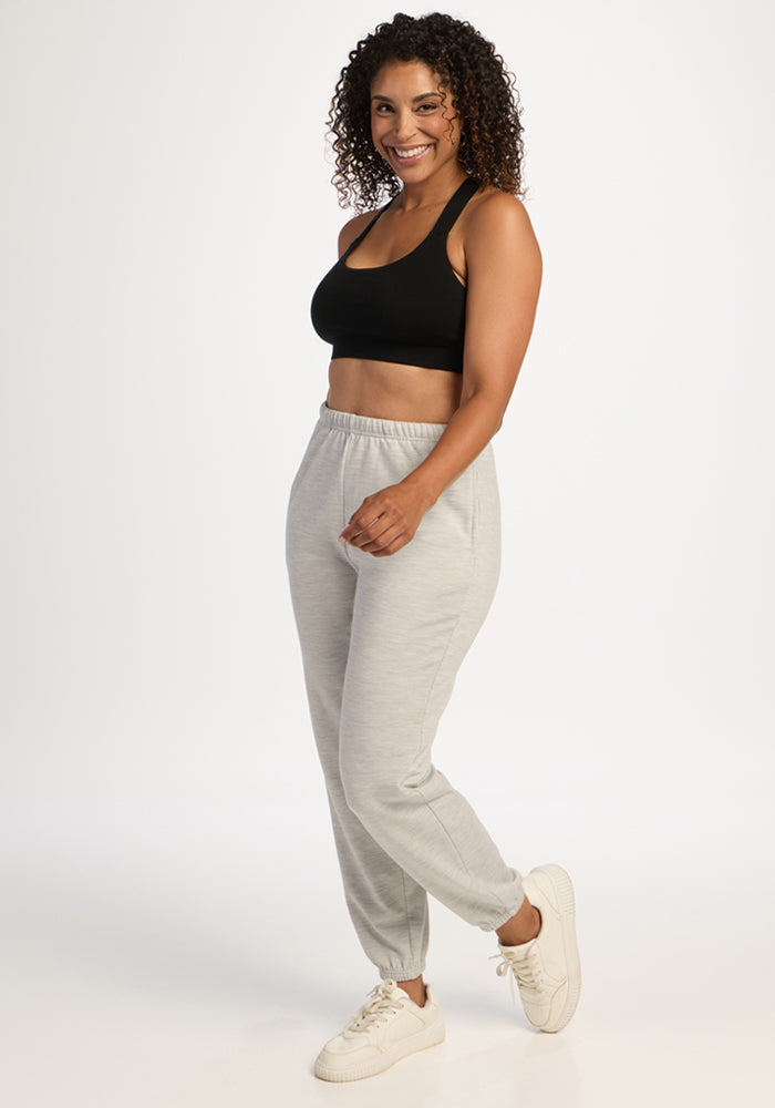 Woman smiling in a black crop top, Woolx Juliette Joggers in Light Ash, and white sneakers against a white background.