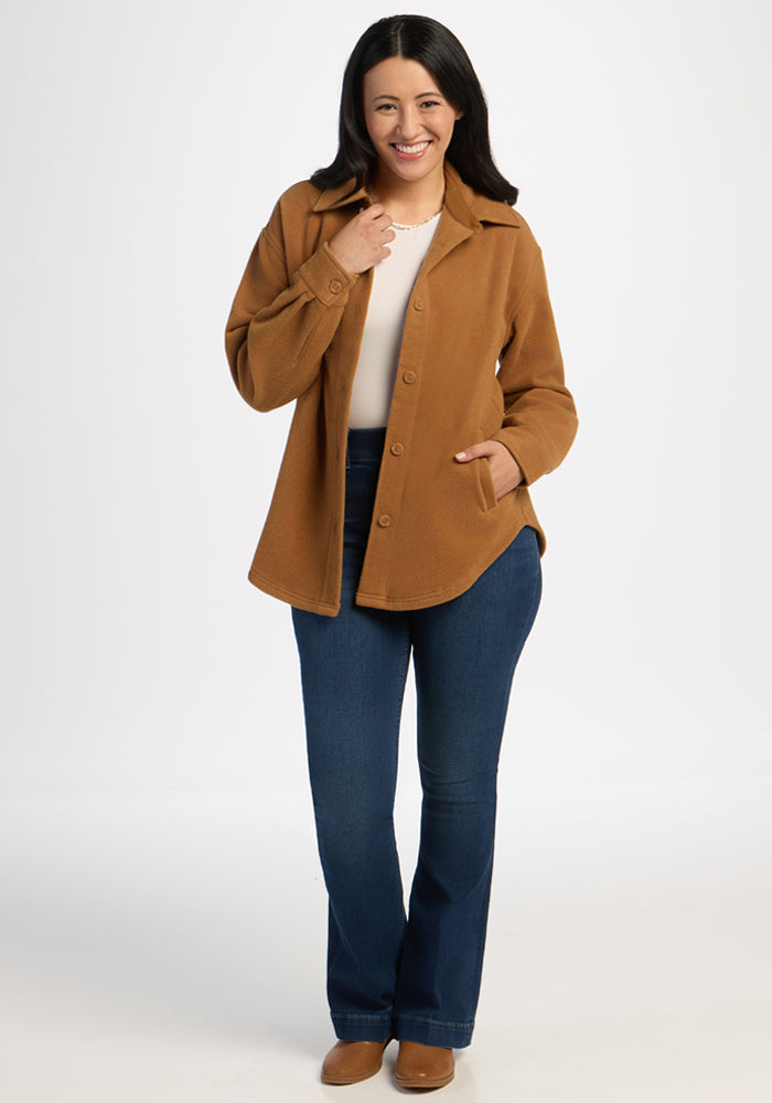 Smiling woman in a Woolx Jovie Shacket - Saddleback, white shirt, and blue jeans stands against a white background.