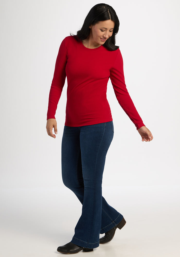 Woman in a Woolx Hadley Ribbed Crew - Maraschino Cherry sweater and blue jeans, smiling as she walks.