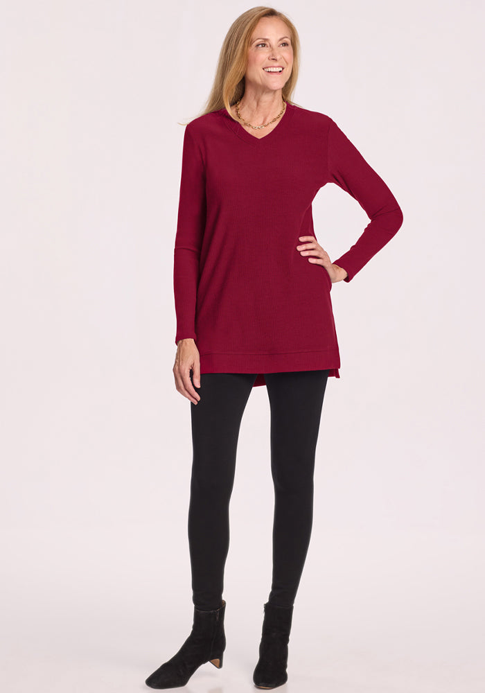 Smiling woman in the Woolx Evie Ribbed Tunic - Beet Red, black leggings, and ankle boots poses with hand on hip.