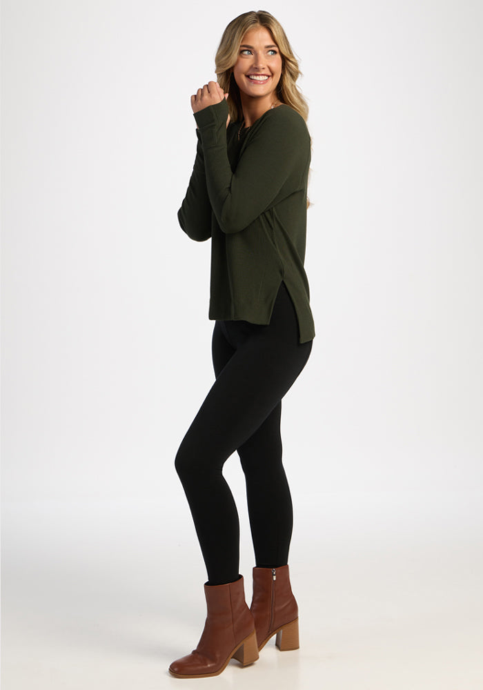Woman smiling sideways in Woolx Ainsley Sweater - Duffel Bag, black leggings, and brown heeled boots.