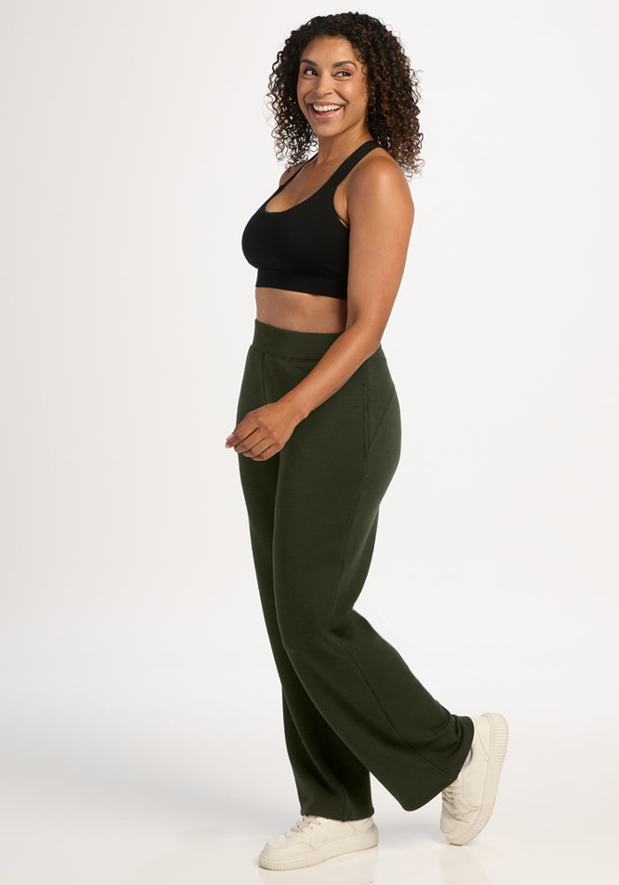 Woman smiling in Woolx Bree Lounge Pants - Duffel Bag and a black crop top with white sneakers against a white background.