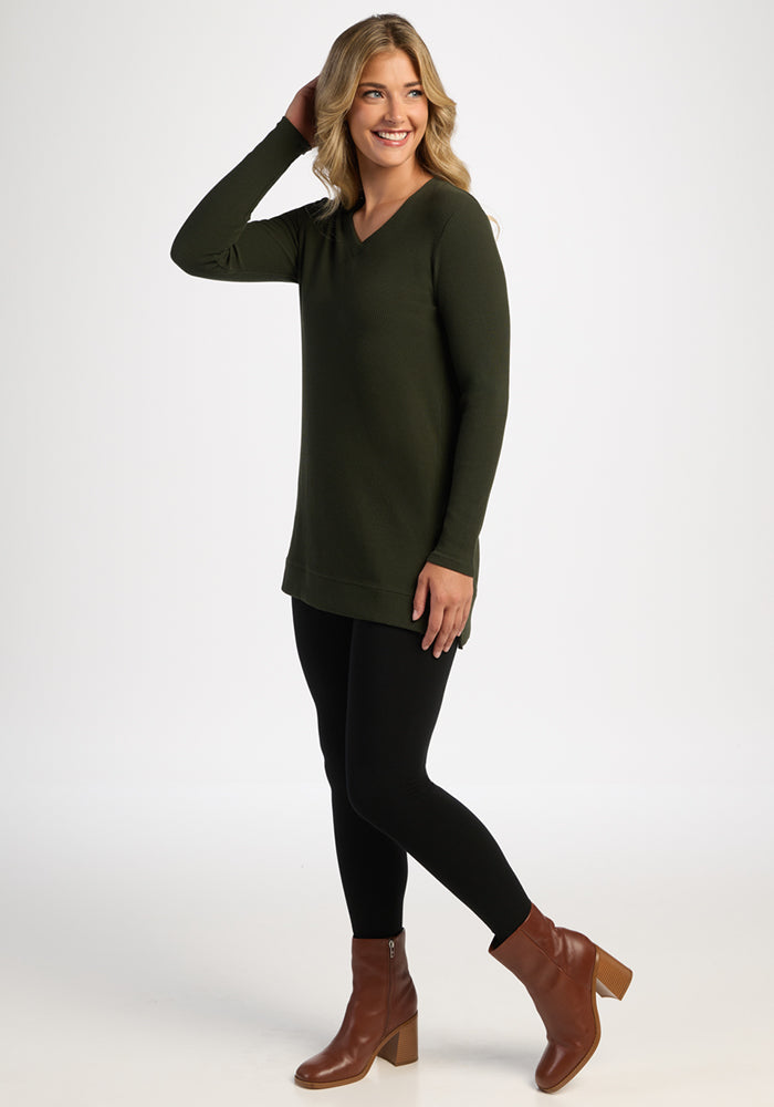 Smiling woman in black leggings models the Woolx Evie Ribbed Tunic - Duffel Bag against a plain white background.