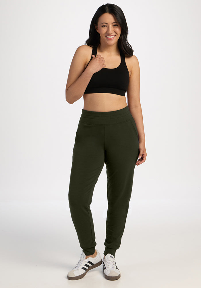 Smiling woman in black sports bra, Woolx Willa Joggers Petite - Duffel Bag, and sneakers stands on white background.