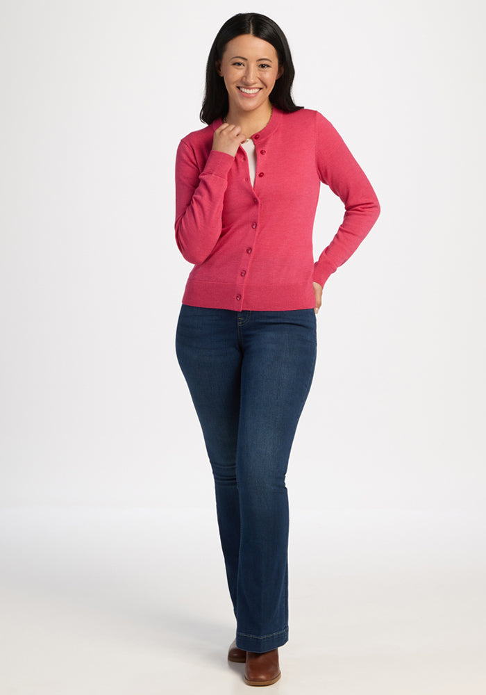 Woman smiling, wearing the Woolx Caitlin Sweater in Vivid Rose, blue jeans, and brown boots on a white background.