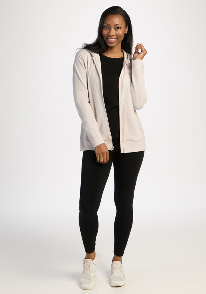 Woman in a Woolx Darby Zip Up Hoodie - Ecru, black shirt, leggings, and white sneakers, smiling confidently.