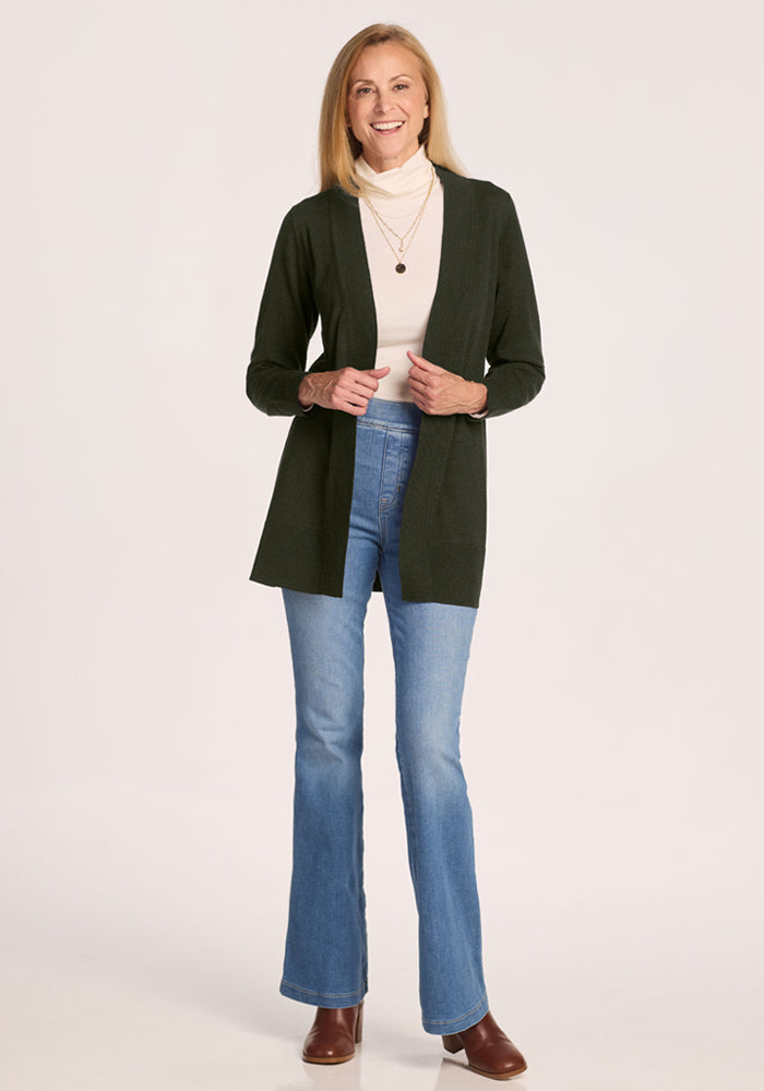Woman in Woolx Macie Sweater - Duffel Bag, white turtleneck, jeans & brown boots stands against a white background.