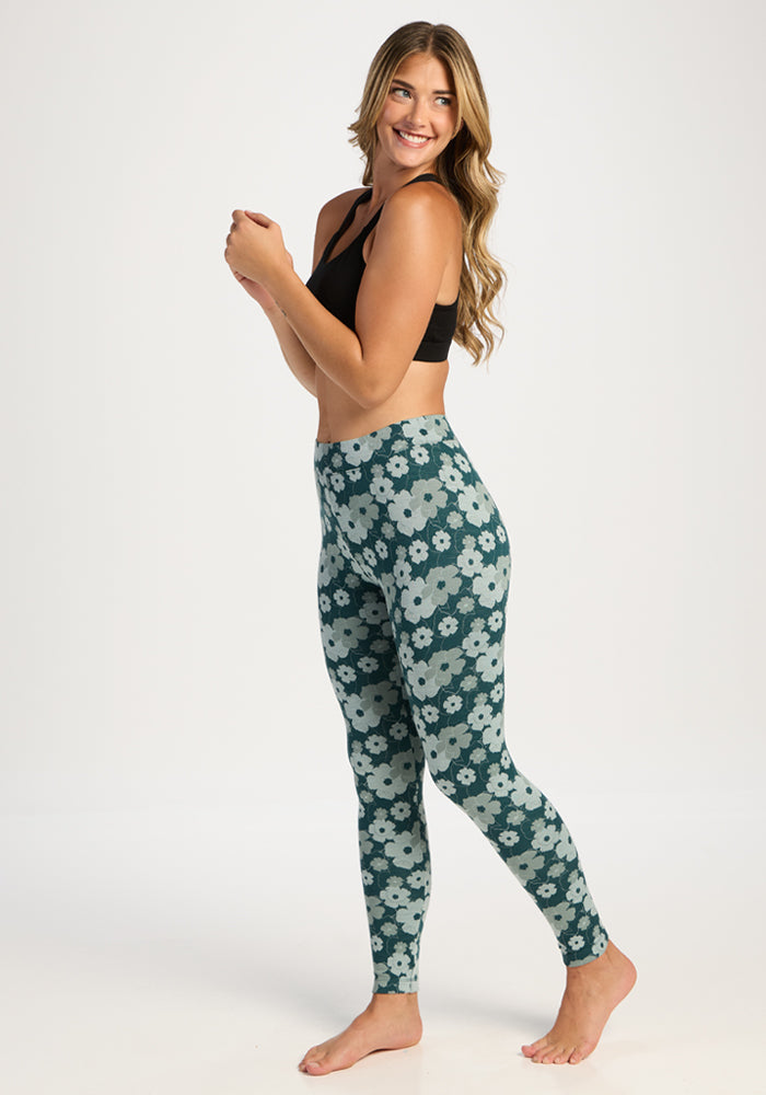 Woman in black sports bra and Woolx Taylor Baselayer Leggings - Coastal Wildflower smiles, standing barefoot.