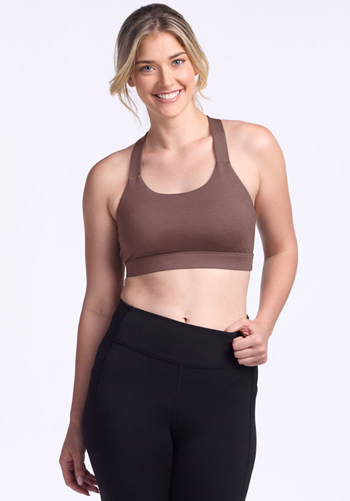 Woman smiles in Woolx Livi Bra - Peppercorn and black leggings against a plain light background. 