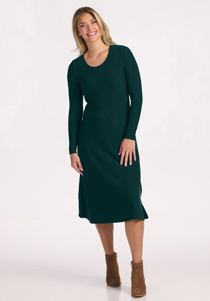 Woman in Woolx Caroline Ribbed Twirl Dress - Deep Pine, smiling in brown ankle boots against a plain background.