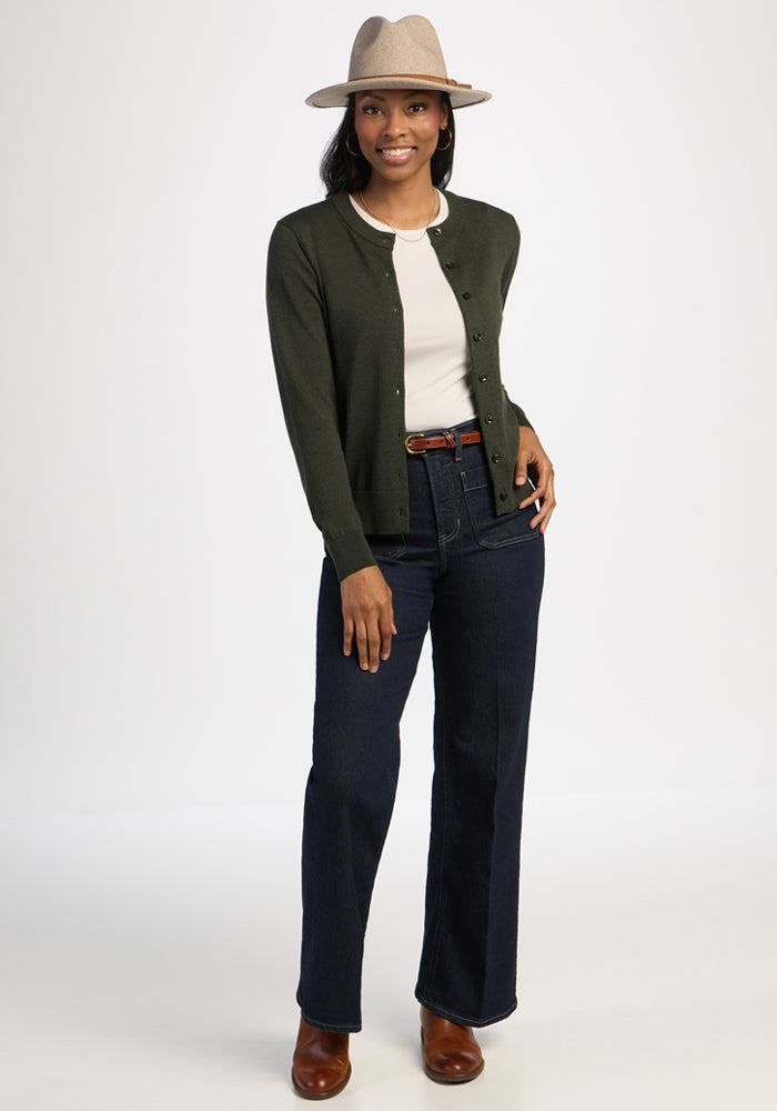 Woman in hat, Caitlin Sweater - Duffel Bag by Woolx, white top, jeans, and brown boots smiles against white background.