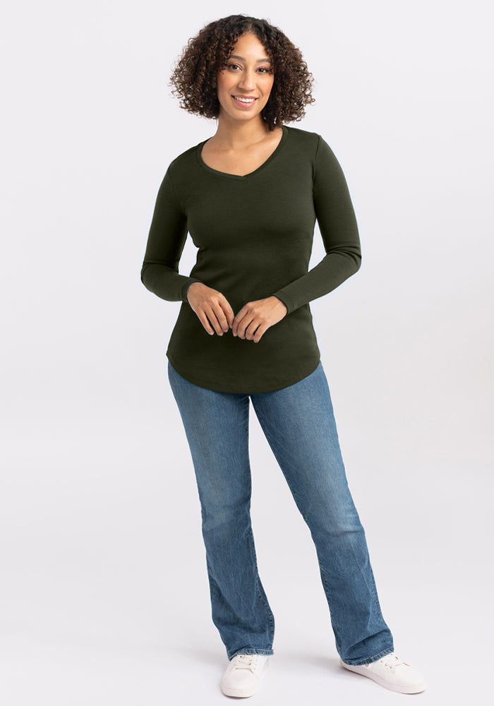 Smiling woman with curly hair wears Woolx Eva Tunic - Duffel Bag, blue jeans, and white shoes.