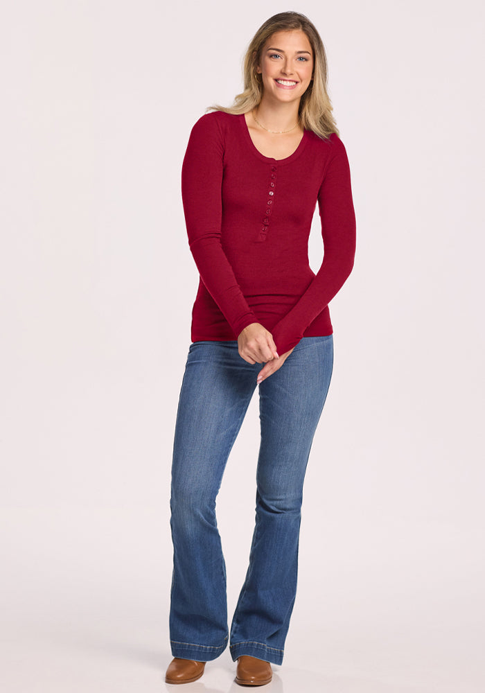 Smiling woman in a Woolx Reese Ribbed Henley - Beet Red and blue jeans stands with hands clasped, facing forward.