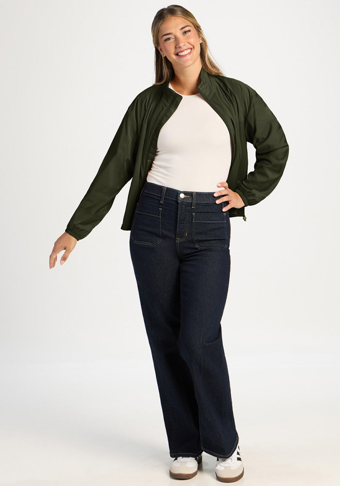 A smiling woman wears a dark green Cooper Windbreaker - Duffel Bag over a white top and dark jeans.