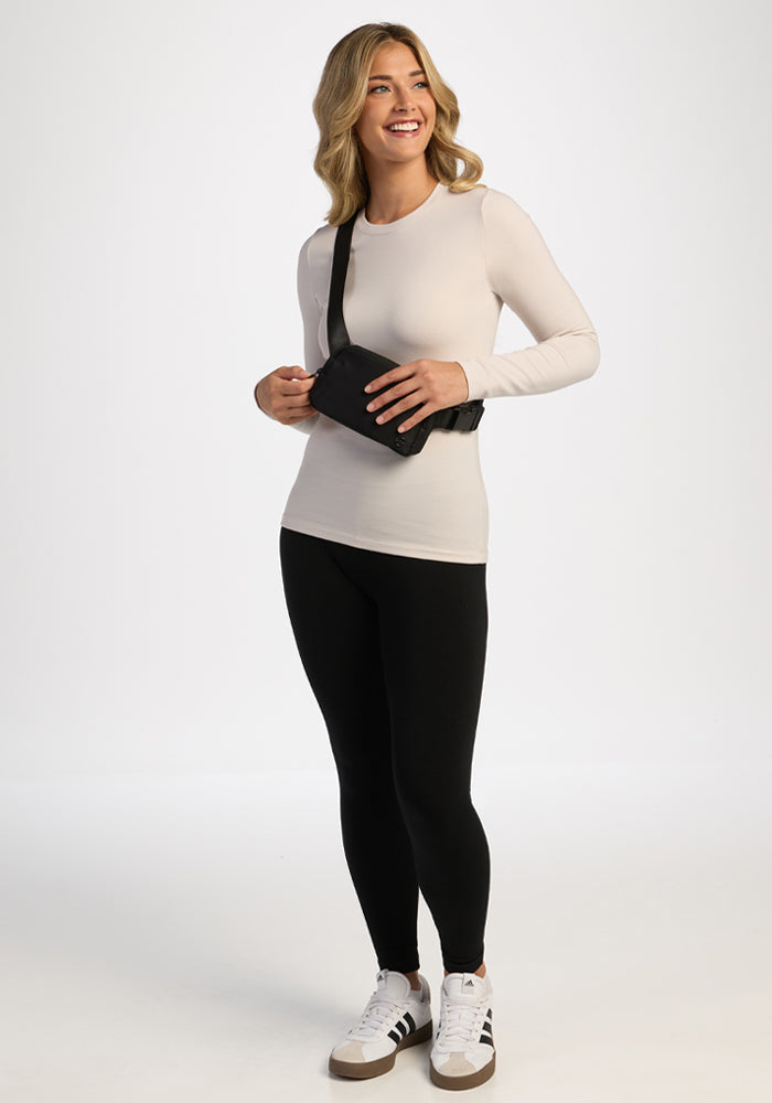 Woman in a Woolx Sadie Baselayer Top - Ecru, smiling and holding a black crossbody bag.