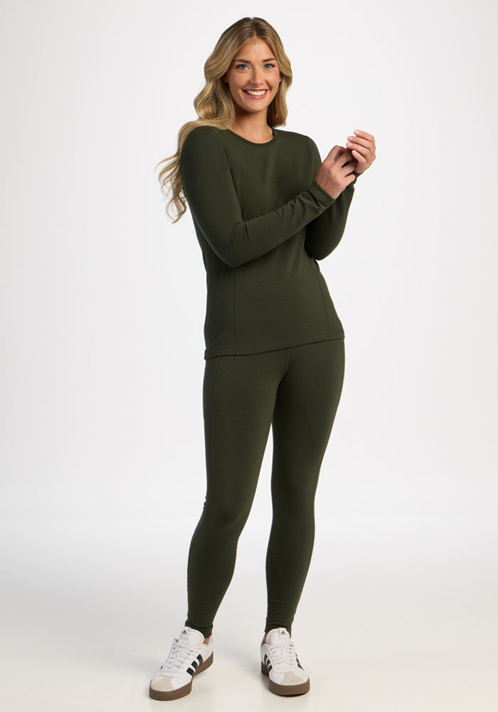 Woman in the Woolx Elsa Long Sleeve - Duffel Bag stands smiling, wearing leggings and white sneakers on plain background.