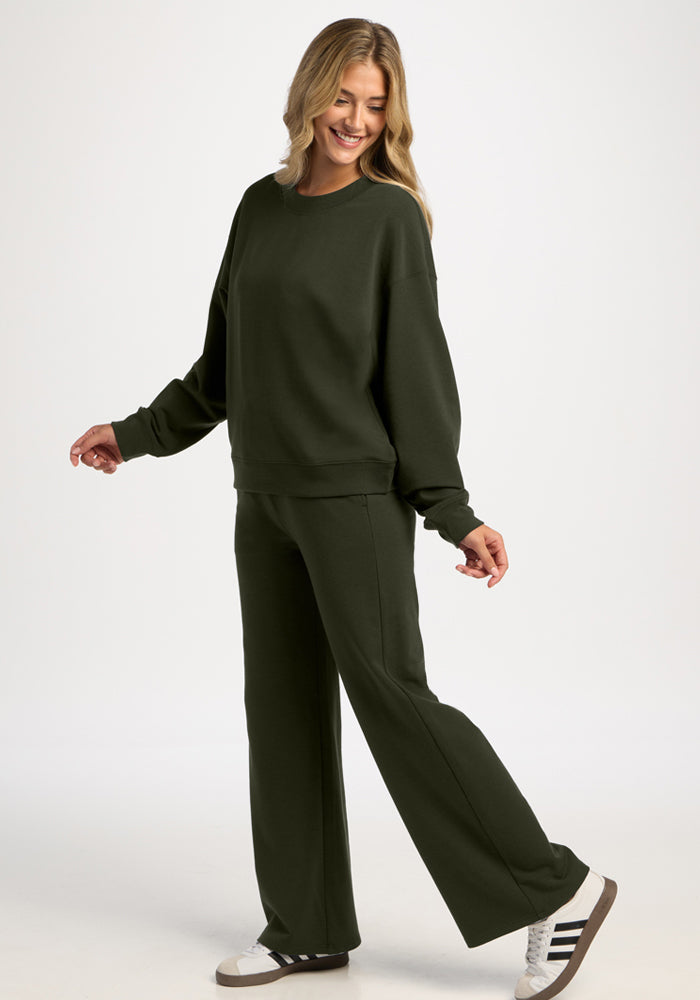 Woman in a dark green Molly Crewneck - Duffel Bag, matching wide-leg trousers, and white sneakers.