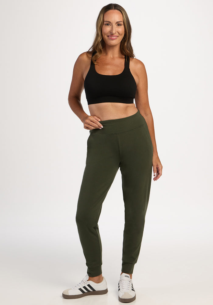 Woman in Woolx Madden Petite Joggers - Everleaf, smiling and posing in a black sports bra against a white background.