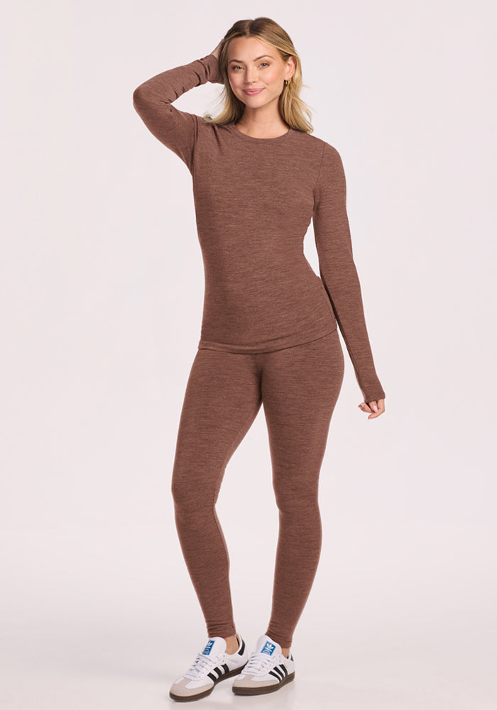 Woman in Woolx Sadie Baselayer Top - Sable Heather, smiling with hand on head, paired with white sneakers.