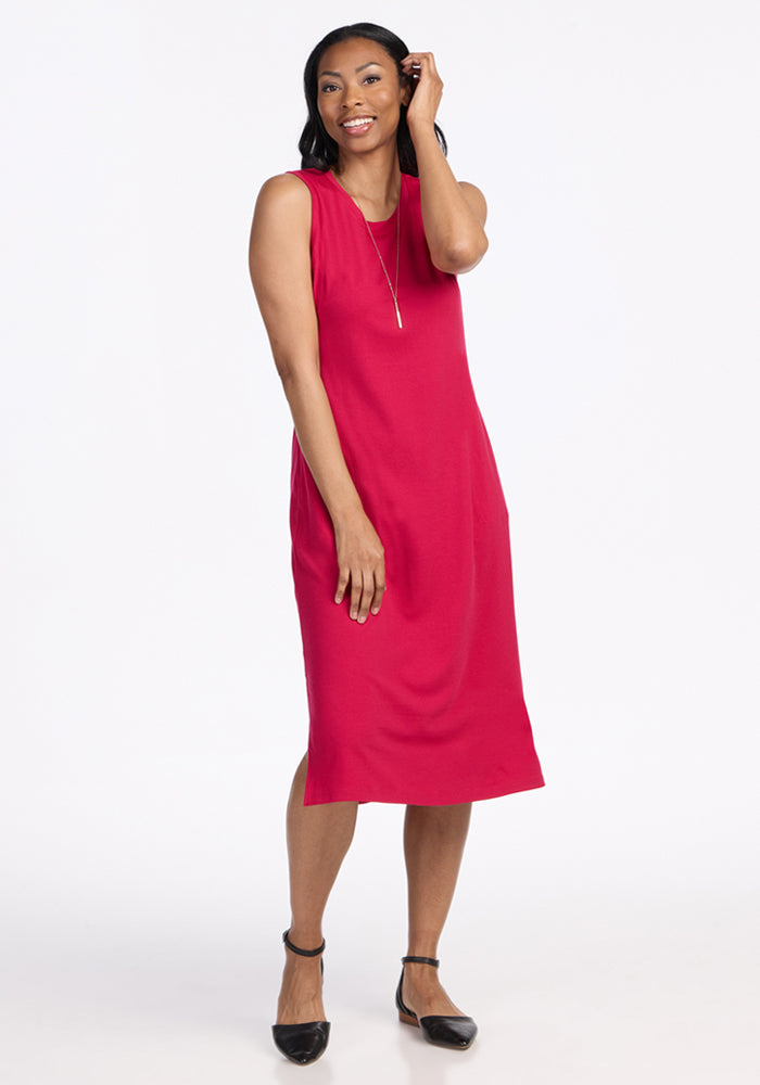 A woman smiles wearing the Woolx Cassie Dress in Poppy Spark, a sleeveless, knee-length Merino wool tank dress, paired with black ankle-strap flats against a plain white background.