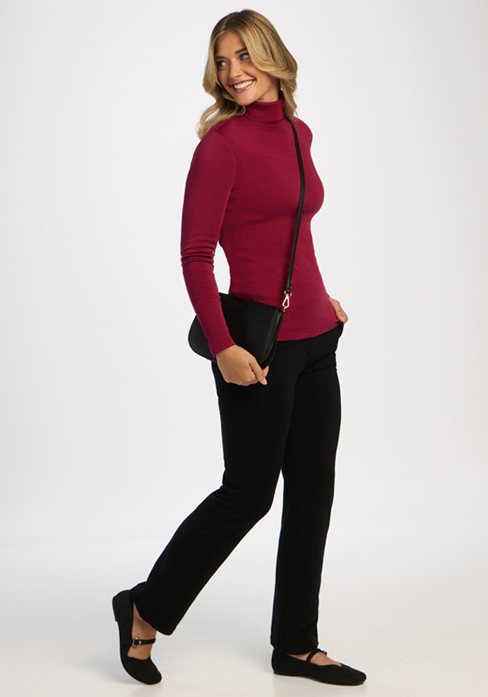 Woman in a Woolx Peyton Turtleneck in Beet Red, black pants, flats, black crossbody, smiling and standing sideways.