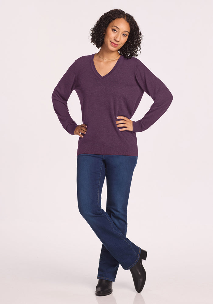Person standing with one knee bent, in Woolx Francesca Sweater - Purple Iris, blue jeans, black boots on white background.