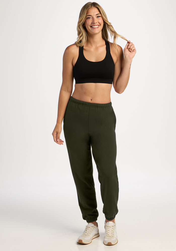 Smiling woman wears Woolx Juliette Joggers - Duffel Bag and a black sports bra against a plain white background.