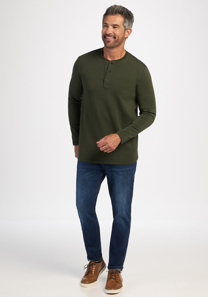 Man in a green Woolx Jackson Henley - Duffel Bag shirt, blue jeans, and brown shoes smiling against a white background.