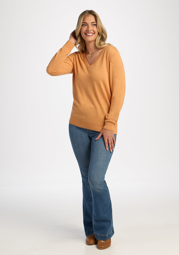 Woman in Woolx Francesca Sweater - Butterscotch, smiling in blue jeans against a white backdrop.