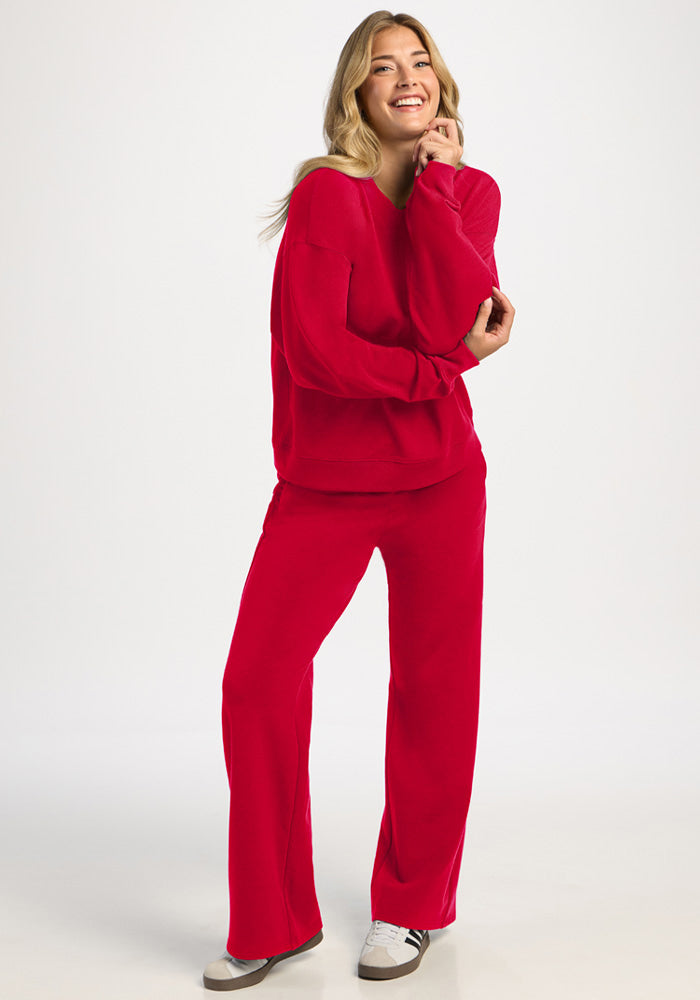 A smiling woman wearing a bright red Molly Crewneck - Maraschino Cherry sweatshirt and matching wide-leg pants.