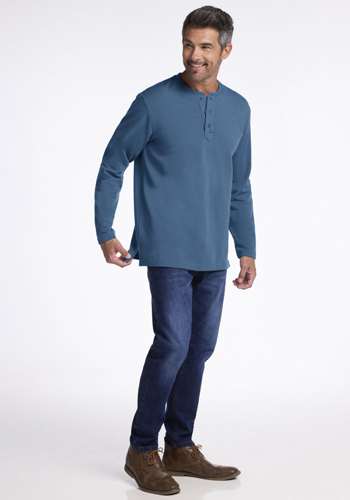 Man in Woolx Jackson Henley - Blue Ashes, jeans, and brown shoes stands smiling against a white background.