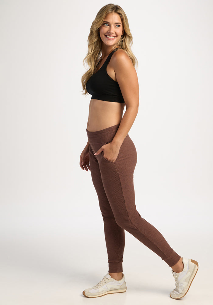 Woman in a black crop top and Woolx Lennon Ribbed Joggers in Sable Heather stands smiling with one hand in her pocket.