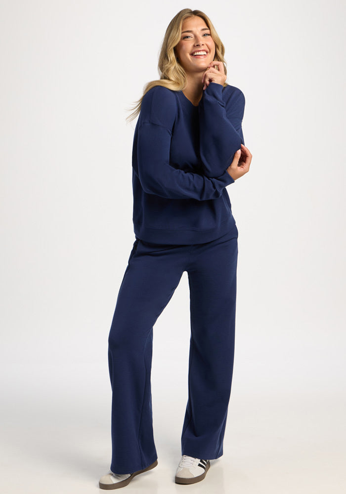 Woman wearing a moisture-wicking Molly Crewneck - Ocean Cavern sweatshirt and matching wide-leg trousers.