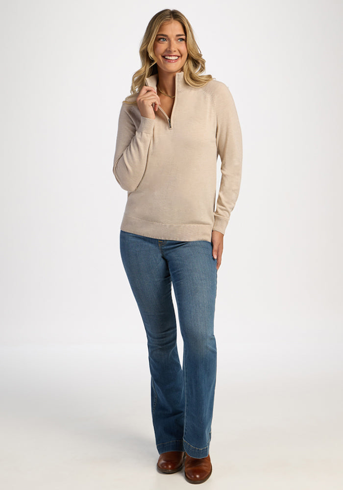 Woman in Woolx Collins Half Zip Sweater in French Oak and blue jeans smiles against a plain white background.