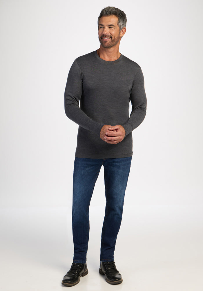 Smiling man in a Woolx Explorer Base Layer - Cinder Melange, blue jeans, and black shoes stands on white background.