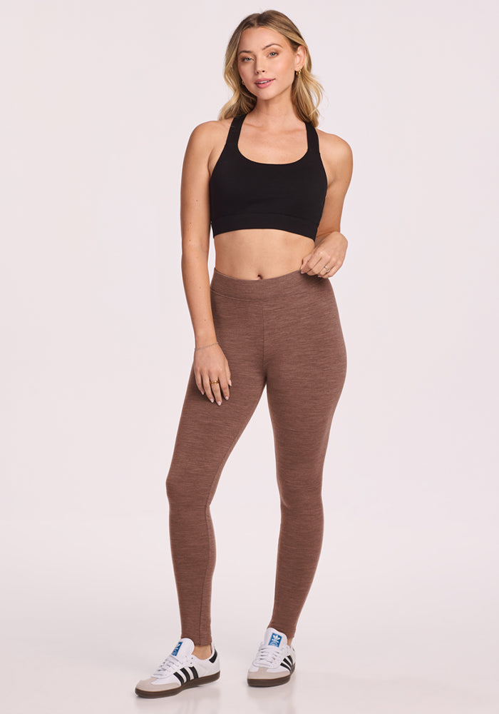 Woman wears Woolx Stella Petite - Sable Heather leggings and a black sports bra, posing in sneakers on a plain backdrop.
