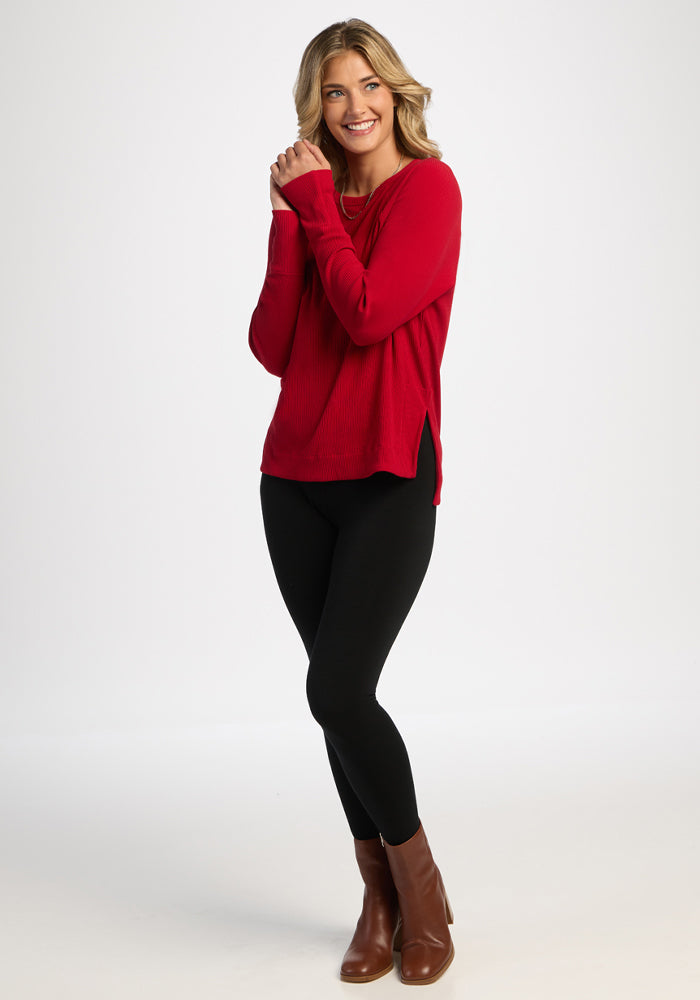 Smiling woman in Woolx Ainsley Sweater - Maraschino Cherry, black leggings, brown boots stands against white background.