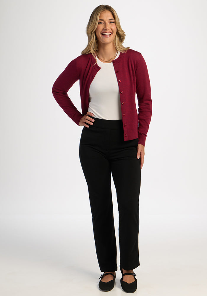 Woman smiling in the Woolx Caitlin Sweater - Beet Red, white top, black pants, and black flats against a white background.
