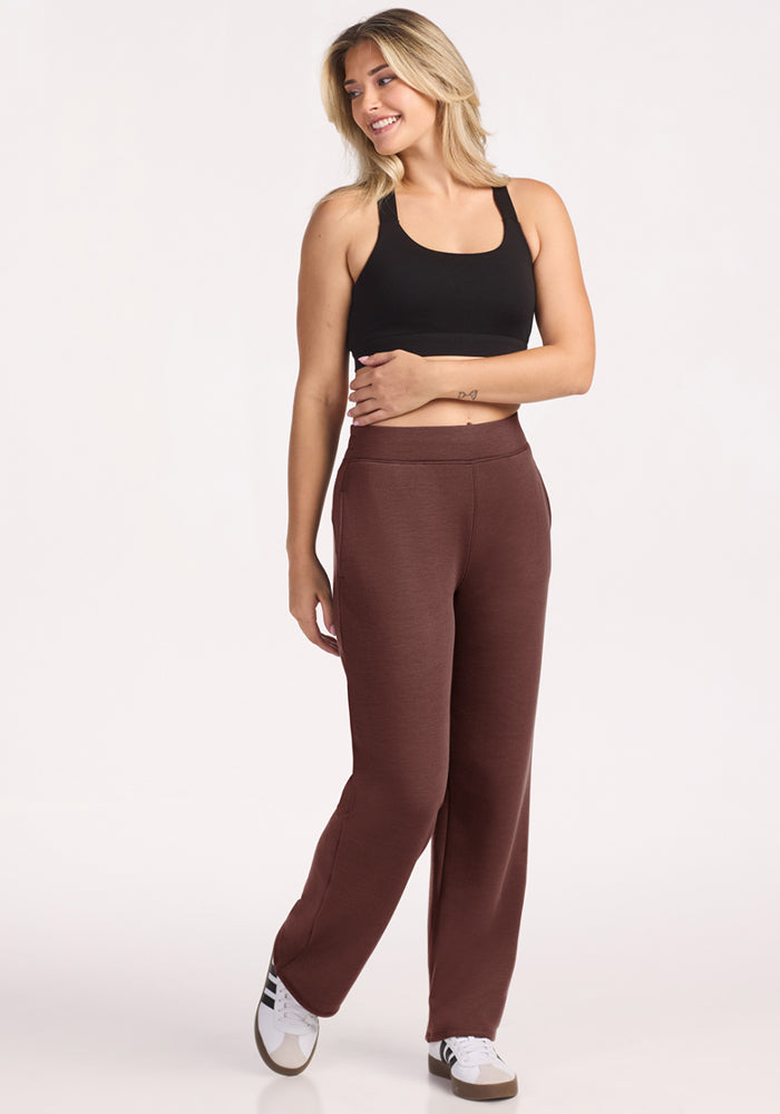 Woman in Bree Lounge Pants - Canyon Clay by Woolx, black tank top, smiles in white sneakers on a plain background.