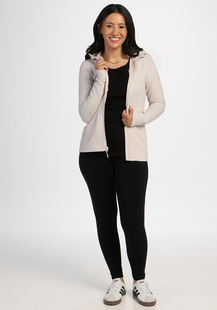 Woman smiles in Woolx Zoey Zip Up Hoodie - Ecru, black leggings, and sneakers against a white background.